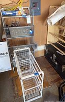 Metal shelving unit with three metal baskets labeled 'THINGS', 'STUFF', and 'EXTRAS' along with white wire basket rack and miscellaneous items