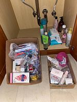 Boxed personal care items including toothpaste, toothbrushes, soap, lotions, and perfume near sink plumbing.