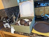 Overall photo showing ceramic tea set in fabric-lined box, Luxa2 stovetop espresso maker box, and black milk steamer with frothing pitcher on countertop.