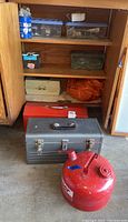Tool boxes inside a wooden cabinet with multiple plastic containers and a bag, and the red gas can on floor.