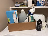 Wooden shelf holding multiple cleaning supply items including gloves, sprays, wipes, and leather restorer bottle.