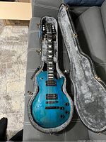 Full view of guitar inside open black hard shell case showing Caribbean Night finish and included strap