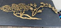 Wide view of one brass wall art piece showing tree branches and flowers design on black background.
