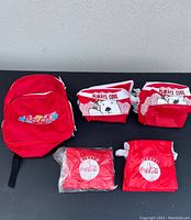 All five items displayed on a table: one red Coca Cola knapsack, two polar bear themed cooler bags, two foldable red Coca Cola bags.