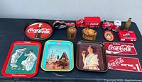 Overview of the entire Coca-Cola collectibles lot showing metal trays, tins, miniature trucks, brass bottle, and advertising signs.
