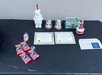 Lot displayed on black table against gray wall showing all items: polar bear figurine, two snow globes, music dome in box, certificates, unopened packs of cards and pogs.