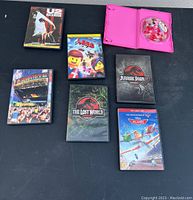 Overview of all seven DVDs arranged on table showing titles and artwork of each DVD case including one pink DVD case open with a red round item inside.