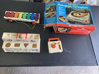 Overview of all toys included in the lot displayed on a black surface: phonograph box, shape sorter, xylophone, and small radio device.