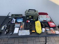 Full view of all items displayed on black table outdoors with fishing gear including tackle boxes, rod and reel, knives, anchor and accessories.