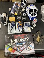 Overview photo showing NHL-OPOLY Junior board game, McFarlane hockey figures, signed hockey pucks, white and blue hockey helmet, pins, and other hockey collectibles spread out on a table.