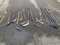 Photo showing 11 hockey sticks laid out on pavement, with varied lengths, colors and designs.