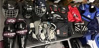 Photo showing assortment of helmets, gloves, pads, skates, and bags arranged on a surface.