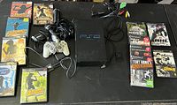 Full lot overview showing PS2 console, controllers, microphones, cables, and games arranged on table.