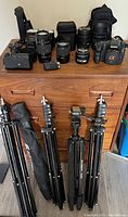 Overview of camera body, lenses, flashes, grip, microphone, and tripods on wooden surface