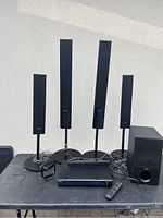 Full view of the 4 Sony tower speakers on stands, subwoofer, receiver, and remote on table