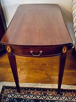 Top view of drop leaf wooden end table with drawer showing wood grain and brass handle on drawer with floral inlay