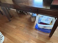 Photo shows wooden desk legs and floor beneath, confirms wood material and style.