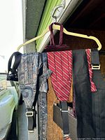 Multiple men's cummerbunds in paisley, stripe, and textured patterns, visible belts, and bow ties hanging on a hanger outdoors.