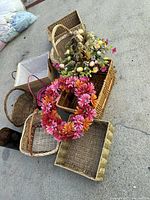 Photo showing multiple woven baskets of various shapes and a pink floral wreath on top of one basket.