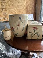 Ceramic bathroom set including soap dispenser, waste basket, and tissue box with floral patterns on beige ribbed ceramic