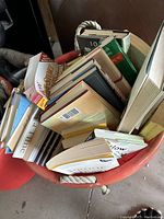 Top view of a bucket filled with assorted hardback and softback books in various sizes and condition.