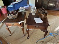 Two Broyhill end tables with Queen Anne style legs, each holding decorative baskets of pine cones and a flower vase on one table and a frosted vase on the other.