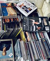 Pile of CDs and DVDs including a Samsung player and music albums 'Muslims'. Various CD cases are stacked horizontally and vertically.