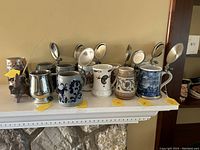 Front view of 11 collectible beer mugs on shelf, various types and designs including ceramic and metal with hinged lids.
