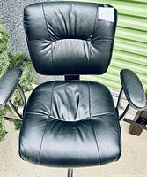 Front view of black office desk chair with cushioned seat and backrest in black faux leather, metal armrests with padded armrest covers