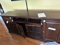 Front view of a dark wood entertainment center with four doors, two solid wood doors on the sides and two glass panel doors in the center, showing wood grain and tags.