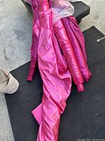 Fuchsia and berry colored fabric rolls with smooth and glossy texture, rolled on tubes, laid on black fabric surface outdoors.