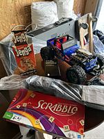 Lot shown on wooden background with white pillows and black bag; items include Scrabble, Jenga, Cards Against Humanity box, and blue RC car.