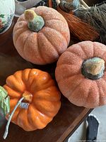 Photo showing three glittery foam pumpkins and one small orange ceramic pumpkin with a green ceramic leaf and brown stem on a wooden surface