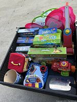 Wide view of all toys in a wicker basket, showing boxed games (Zingo, Super Bubbles, Word Launch), butterfly toy, piano toy, and various educational toys