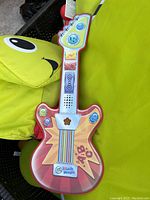 Red toy guitar with multiple colored buttons and star design on body.
