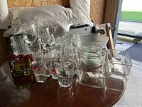 Collection of various clear and colored glass kitchenware including glasses, containers, bowls, and plates on a round table.