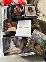 Box filled with DVDs, CDs, and cassettes with visible titles Joan of Arc, Sicario, The Color of Paradise, Dolomite Is My Name among others.