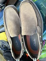 Pair of men's Clarks suede loafers in light tan/gray color with visible wear.