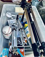 Container holding three tripods, baseball, candles, and various small items