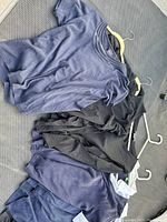 Photo showing multiple women's tops and jackets in navy blue and black laid out on floor, hung on white hangers.
