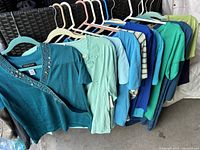 Collection of women's tops on hangers in mostly blue, teal, and green tones highlighting styles and fabric details