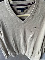 Light gray Tommy Hilfiger V-neck sweater showing the logo and size tag.