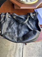 Large black leather purse with gold chain and buckle detail on a wooden table