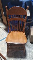 Front view of one wooden dining chair showing carved top backrest, spindles, and solid wood seat.
