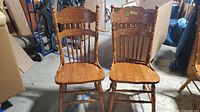 Front view of two wooden dining chairs showing carved top rail, spindle backrest, and solid wooden seats.