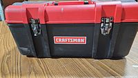 Front view of closed Craftsman toolbox showing red and black plastic construction with metal latches and Craftsman logo.
