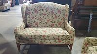 Front view of vintage floral love seat couch with padded armrests and wood legs.