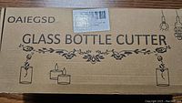 Closed cardboard box labeled Oaiegsd Glass Bottle Cutter with floral design and bottle candle illustrations