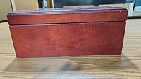 Rectangular wooden humidor box with reddish-brown finish, damage and scratches visible on one side.