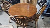 Round wooden dining table with four chairs around it, showing wood grain and general condition.